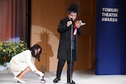 サングラスと正賞のブロンズ像を床に置き、眼鏡と松尾スズキ「老人賭博」(文春文庫)を取り出すケラリーノ・サンドロヴィッチ。