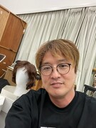 ウィッグをバックに笑顔の酒井。髪がボサボサなのは、カツラ合わせの直後だから。