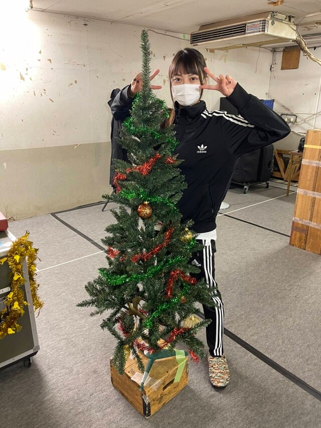 ライン入りのadidasジャージーでスマートな印象に。舞台美術のクリスマスツリーを前にピース。