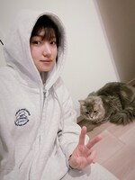 活発な印象の、ロゴ入りのパーカ姿でピース。後ろは太田のピースに釘付けの愛猫。