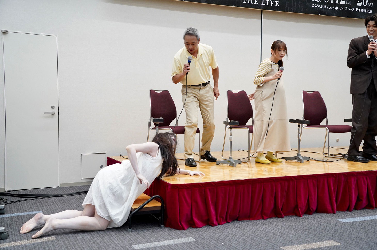 這いつくばって壇上に登る、佐々木心音扮する佐伯伽椰子（左）と、逃げるいしだ壱成（中央左）と大場美奈（中央右）。