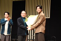 万城目学（中央）の直木賞受賞を祝い、花束を手渡す中川大輔（右）。