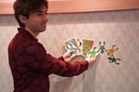 「AiRK Research Project vol.2 山田悠 + サム・ワイルド 2人展『Walls ans Frogs -境界線に見るあわい-』」より、カエルのステッカーを見せるサム・ワイルド。