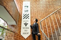 giraffeのWORK TO SHOP Sendagayaの看板前にて。ビシッと決まったスーツ姿で、ネクタイ型看板を見上げる米吉。なおWORK TO SHOP Sendagayaは現在夏季休業中。10月初旬より営業再開予定。