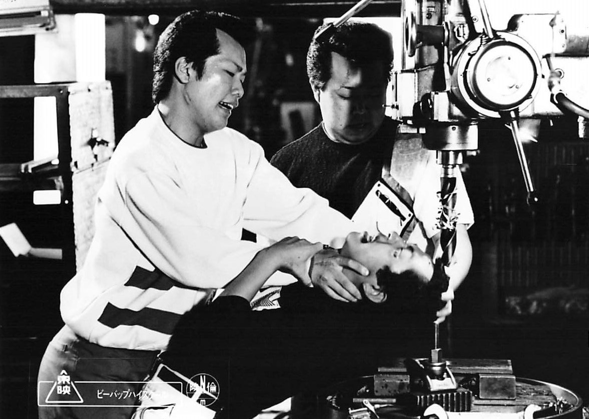 映画2作目「ビー・バップ・ハイスクール 高校与太郎哀歌」より。左が白井光浩演じる、テルこと藤本輝男。ケンコバがここで2度もモノマネしているのは、「城東なんて数の多いチンピラの集まり」という陰口をたまたま聞いたテルがブチ切れ、シンペーの顔をドリルで貫こうとするシーン ©︎東映