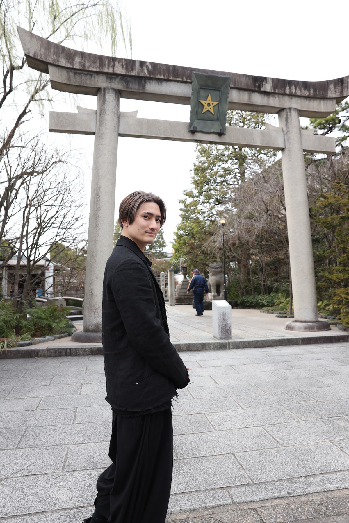晴明神社の一の鳥居の前に立つ中村隼人。金色の「晴明桔梗」（通称「五芒星」）が掲げられている。