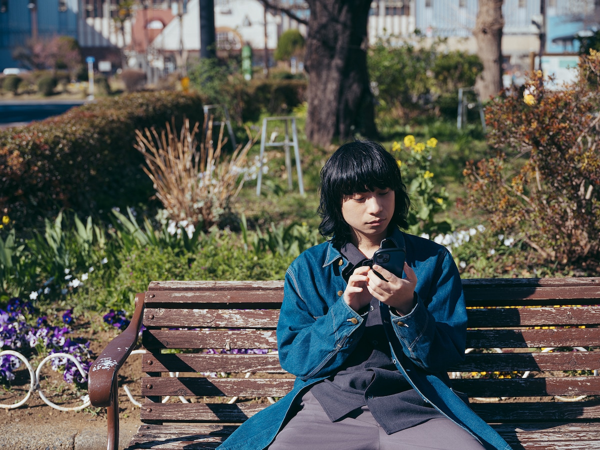 国立駅付近のベンチに座って音楽を聴く尾崎世界観。